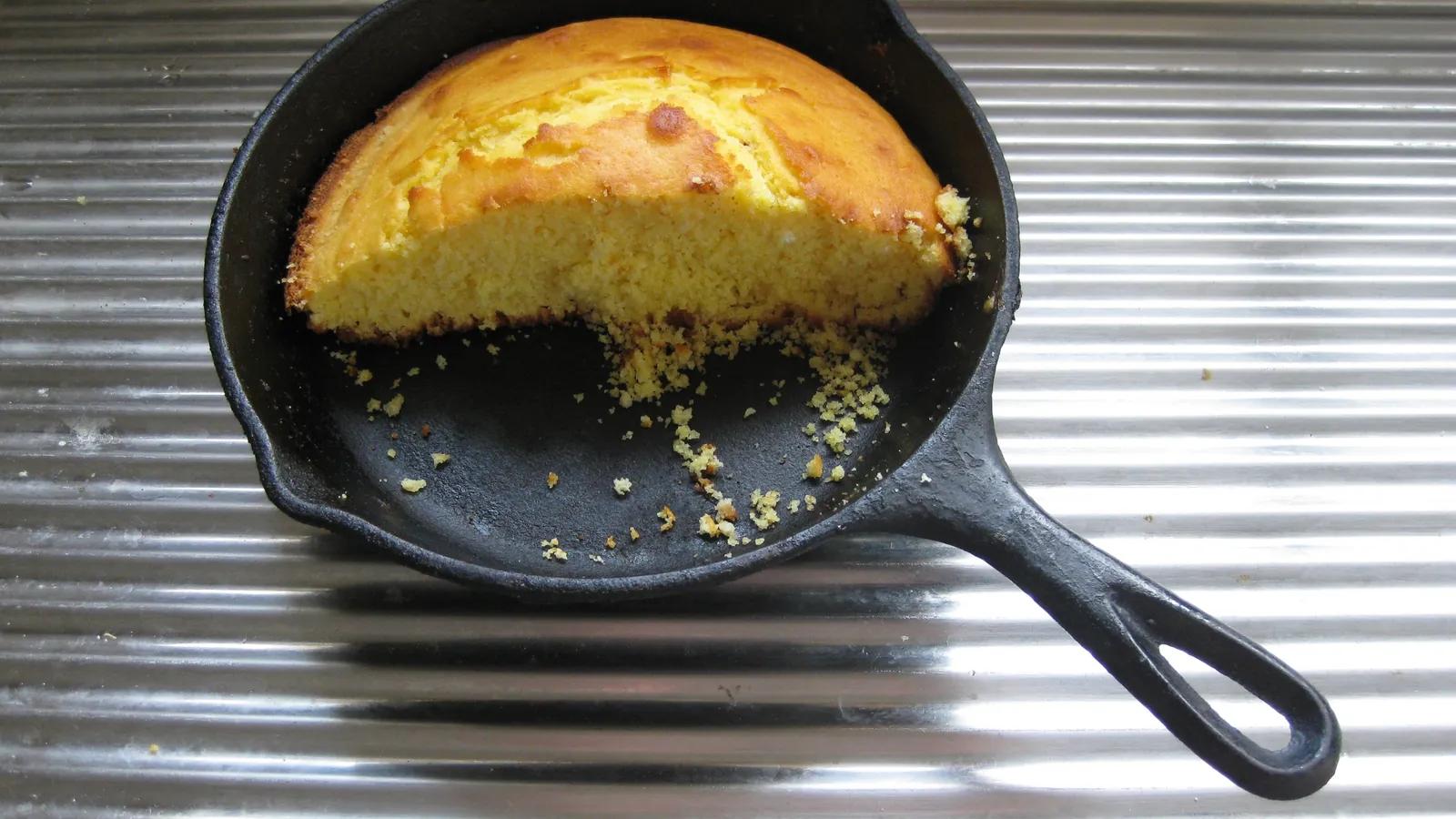 Golden cornbread baked in a black cast iron skillet, with a wedge cut out