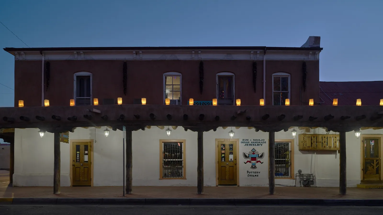 An adobe shop on the plaza in Old Town Albuquerque lined with glowing luminarias at dusk during the holiday season