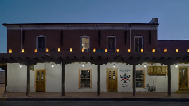 An adobe shop on the plaza in Old Town Albuquerque lined with glowing luminarias at dusk during the holiday season