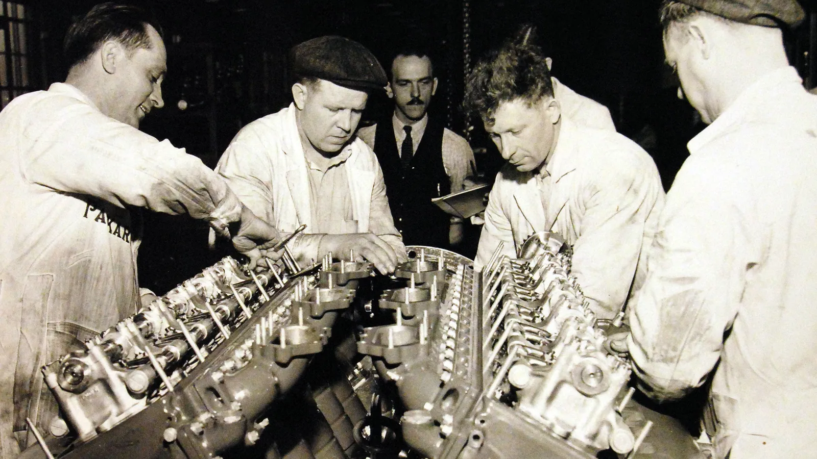 Four machinists in work clothes assemble the supercharger on a large V-12 marine engine at the Packard plant in Detroit in 1941