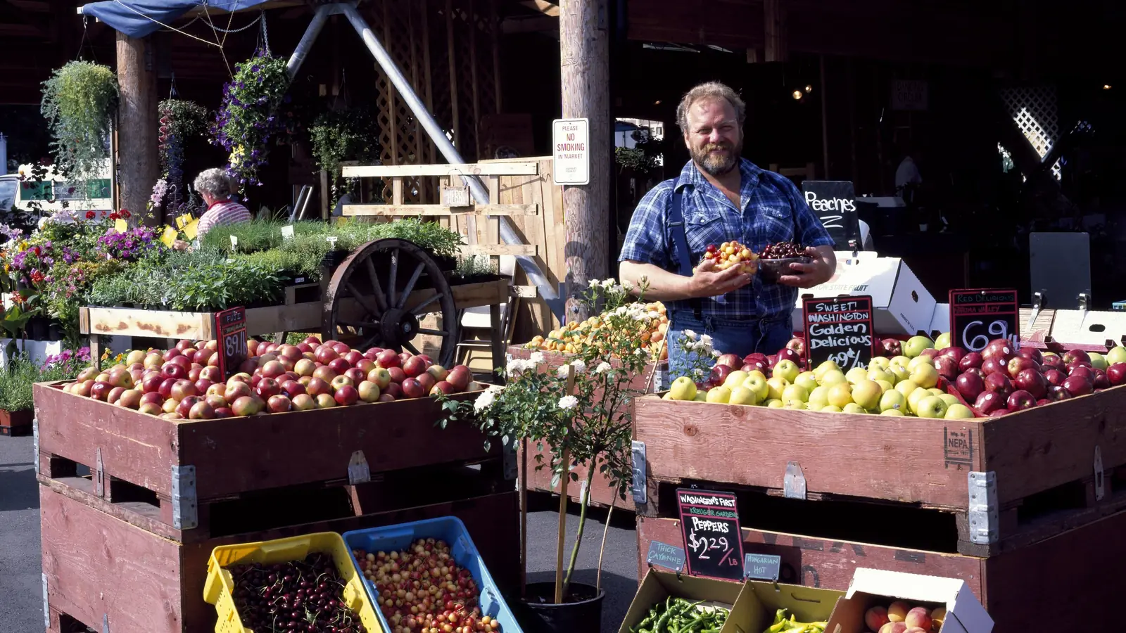 A vendor stands behind wooden crates of apples, pears, peppers and greens at his stall at the Olympia Farmers' Market in Washington state