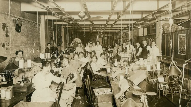 Rows of seamstresses work at sewing machines in a large, bright garment workshop in St. Louis in 1919