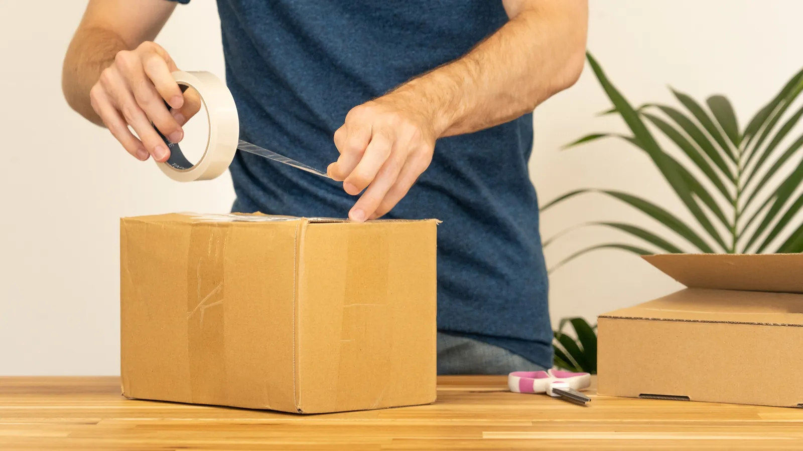 A man sealing a cardboard shipping box with packing tape on a work table