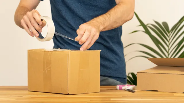 A man sealing a cardboard shipping box with packing tape on a work table