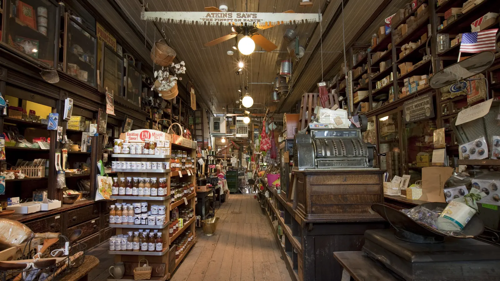 Wooden shelves stocked with goods inside Harrison Brothers Hardware, a historic store in Huntsville, Alabama, with an American flag hanging overhead
