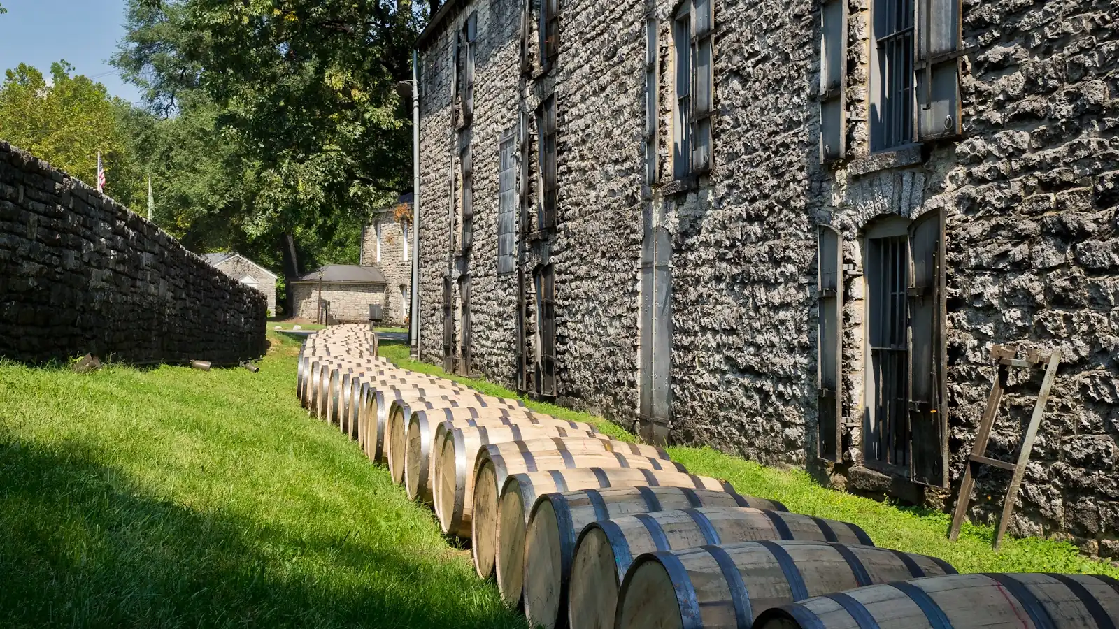 Rows of freshly filled oak bourbon barrels lined up outside a stone rickhouse at a Kentucky distillery
