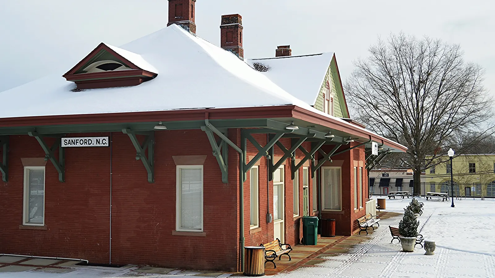 Red-brick Sanford, N.C. railroad depot with green brackets and benches along a snowy platform