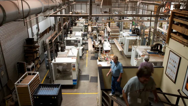A factory floor lined with automated CNC milling machines, with a few workers walking between them