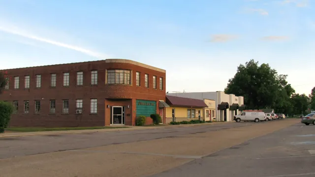 A two-story red brick building and low storefronts along a quiet street in South Pittsburg, Tennessee, under a blue evening sky